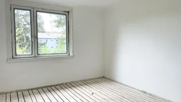 Leerer Raum mit einem Fenster, das einen Blick auf Bäume und ein entferntes Gebäude freigibt.