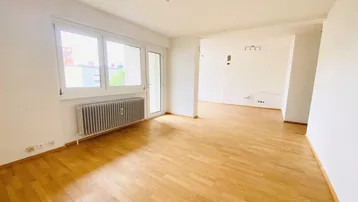Helles Wohnzimmer mit Parkettboden, großem Fenster und Zugang zum Balkon.