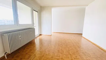 Helles Wohnzimmer mit Fischgrätparkettboden und Zugang zu einem Balkon.