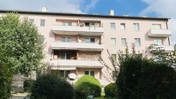 Mehrfamilienhaus mit mehreren Balkonen und gepflegter Grünanlage im Vordergrund.
