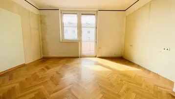 Heller Wohnraum mit Fischgrätparkett und direktem Zugang zu einem Balkon.