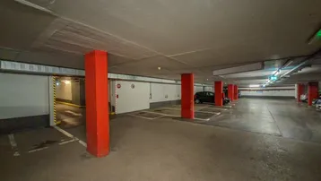 Geräumige Tiefgarage mit markierten Stellplätzen und roten Säulen, gut beleuchtet.