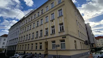 Mehrstöckiges Wohngebäude mit gelber Fassade und klassischen Fenstern an einer Straßenecke in der Stadt.