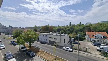 Weitläufiger Blick von oben auf die belebte Straße, umliegende Gebäude und grüne Bäume.