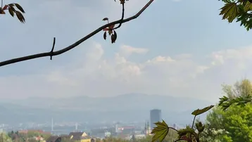 Panoramablick über eine grüne Hügellandschaft mit einer Stadt und Bergen im Hintergrund.