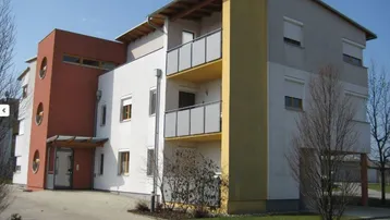 Modernes Mehrfamilienhaus mit farbigen Akzenten, Balkonen und Rollläden an den Fenstern.