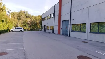 Außenansicht eines Gewerbegebäudes mit großem Parkplatz und umgebender Natur unter blauem Himmel.