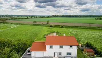 Luftaufnahme des Hauses mit rotem Dach, umgeben von grünen Feldern und einem Teich.
