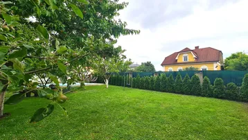Gepflegter Garten mit Rasenfläche, Obstbäumen und Blick auf ein charmantes Haus mit Satteldach.