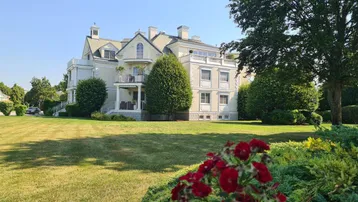 Elegante Villa mit weitläufigem Rasen und gepflegter Gartenanlage unter blauem Himmel.