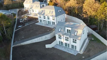 Moderne Neubau-Doppelhäuser mit Mansarddächern und großen Fenstern in einer sich entwickelnden Wohnsiedlung.