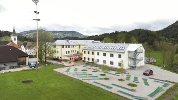 Luftaufnahme eines Hotelkomplexes mit Minigolfanlage, umgeben von grünen Hügeln und einem Dorf.