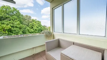 Möblierter Balkon mit Blick ins Grüne und bequemen Sitzgelegenheiten unter blauem Himmel.