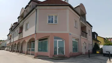 Mehrstöckiges Eckgebäude mit Gewerbeflächen im Erdgeschoss und Wohnungen darüber, an einer Straße gelegen.