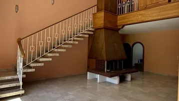 Geräumiges Wohnzimmer mit großem Kamin, Marmorboden und offener Treppe zum Obergeschoss.