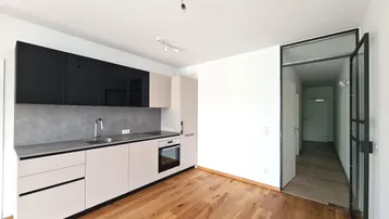 Moderne Einbauküche mit schwarzen Oberschränken und hellem Holzfußboden, offen zum Flur.
