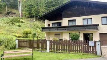 Charmantes Haus in ländlicher Umgebung mit Holzbalkon und Blick auf bewaldete Hügel.