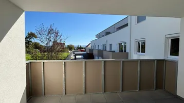 Geräumiger Balkon mit Fliesenboden und Blick auf die umliegenden Gebäude und Grünflächen.