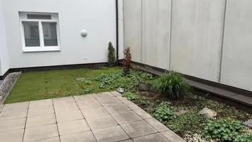 Kleine gepflasterte Terrasse mit angrenzendem Gartenbereich und Blick auf die Gebäudefassade.