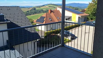 Balkon mit weitem Blick über die ländliche Umgebung, Häuser und ferne Hügel.