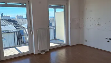 Heller, leerer Raum mit Laminatboden, Heizkörper und Zugang zu einem Balkon mit Dachblick.