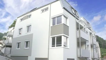 Modernes Mehrfamilienhaus mit weißer und grauer Fassade sowie mehreren Balkonen unter blauem Himmel.