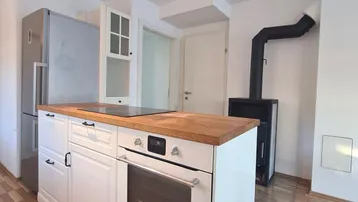 Kücheninsel mit integriertem Backofen und Kochfeld, daneben ein moderner Holzofen.