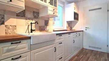 Helle Küche mit weißen Schränken, Holztheke, Bauernspüle und gemustertem Fliesenspiegel.