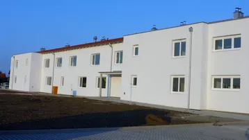 Neues Wohngebäude mit weißer Fassade, vielen Fenstern und noch unfertigem Außenbereich.