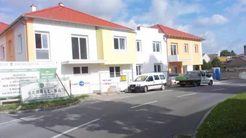 Neue Wohngebäude mit farbigen Akzenten und rotem Dach, umgeben von einer Baustelle.