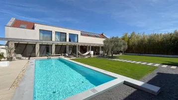 Modernes Haus mit großem Garten, Swimmingpool und Sonnenterrasse unter blauem Himmel.