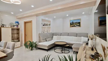 Modernes Wohnzimmer mit beigem Ecksofa, hellen Fliesen und indirekter Deckenbeleuchtung.