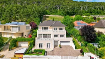 Repräsentative Villa mit gepflegtem Garten und Auffahrt, umgeben von grünen Hügeln und Wald.