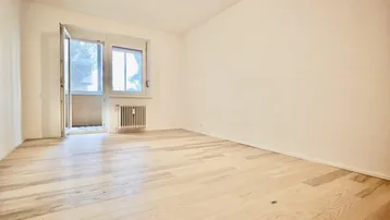 Helles Zimmer mit hellem Holzfußboden und Zugang zu einem französischen Balkon.