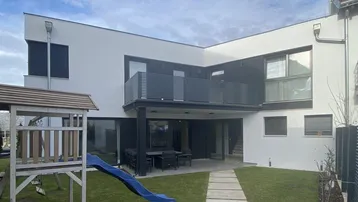 Moderne Hausfassade mit Garten, Rasenfläche und Kinderspielplatz im Hinterhof.