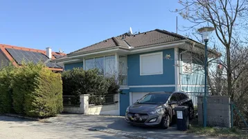 Blaues Einfamilienhaus mit Satteldach, Vorgarten und geparktem Auto auf der Einfahrt.