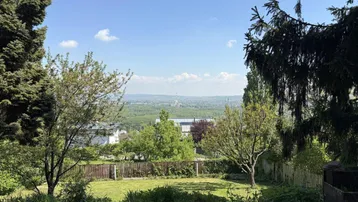 Gartenbereich mit weitem Blick über die Landschaft und Bäumen unter blauem Himmel.