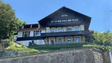 Traditionelles Haus mit mehreren Balkonen und Blick auf die umliegende Natur unter blauem Himmel.