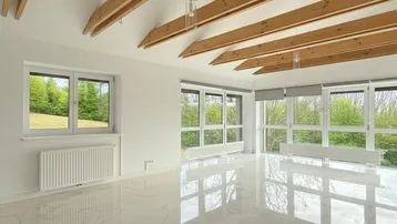 Helles Wohnzimmer mit glänzendem Fliesenboden, Holzbalken und weitem Blick ins Grüne.