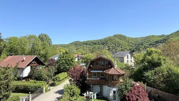 Weitläufiger Blick auf das Haus und die umliegende grüne Hügellandschaft unter blauem Himmel.