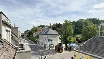 Blick von einem Balkon auf eine Straße, umliegende Gebäude und grüne Hügel in der Ferne.