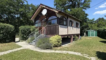 Kleines Holzhaus mit Satteldach und Garten in ländlicher Umgebung unter blauem Himmel.
