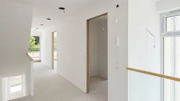 Heller Flur mit Treppenaufgang und Blick ins Grüne durch die Fenster.