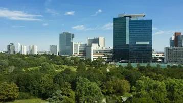 Panoramablick auf die moderne Skyline einer Stadt mit grünen Parkanlagen unter blauem Himmel.