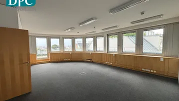 Großer, runder Büroraum mit vielen Fenstern, Teppichboden und Holzvertäfelung, ideal für offene Arbeitsbereiche.