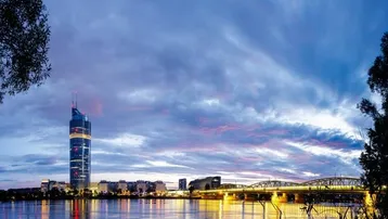 Panoramablick auf die beleuchtete Stadt bei Sonnenuntergang mit Fluss und Brücke.