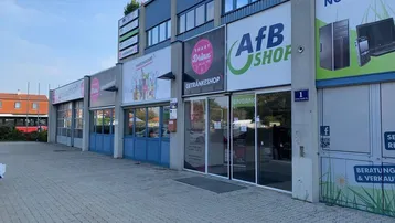 Ansicht eines modernen Geschäftsgebäudes mit mehreren Ladenfronten und großen Fenstern im Obergeschoss.