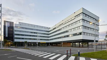 Modernes Bürogebäude mit markanter Architektur, großen Fensterfronten und einem weitläufigen Parkplatzbereich.