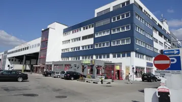 Ansicht eines modernen Büro- und Geschäftsgebäudes mit blauer und weißer Fassade sowie Parkplätzen davor.