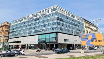 Modernes Bürogebäude mit Glasfassade und vielen Fenstern an einer belebten Straße.